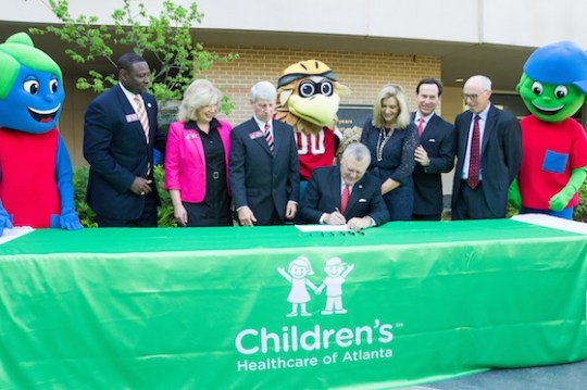 Gov. Nathan Deal signs the Return to Play Act into law as state lawmakers, Children's Healthcare of Atlanta officials, Falcons president Rich McKay and team mascot Freddie the Falcon look on, along with Children's mascots